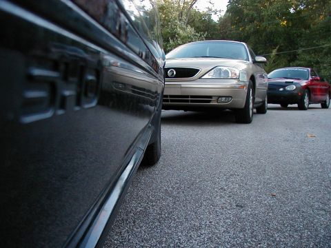1990 Ford Taurus - Three cars parked in a row, with a dark car in the foreground and a gold Mercury Sable and red car behind it.