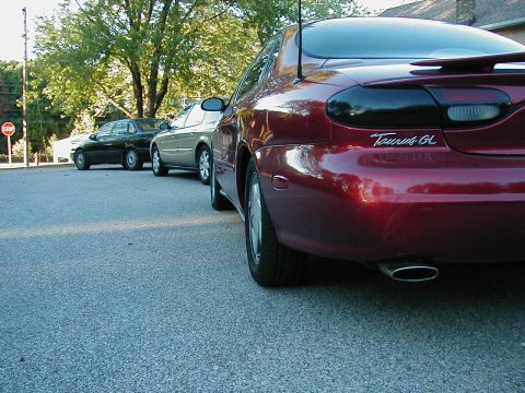 1990 Ford Taurus - A red 1990 Ford Taurus GL is parked behind two other vehicles on a street.