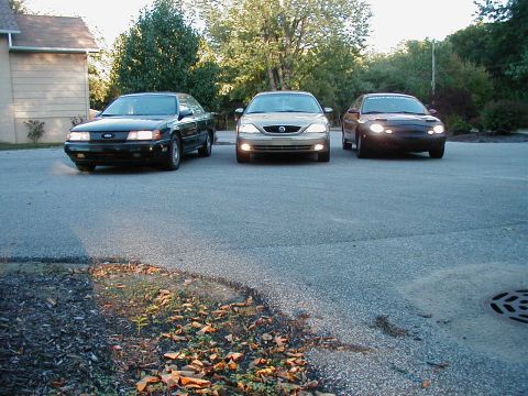 1990 Ford Taurus - Three sedans parked in a driveway, including a 1990 Ford Taurus and a Mercury Sable.