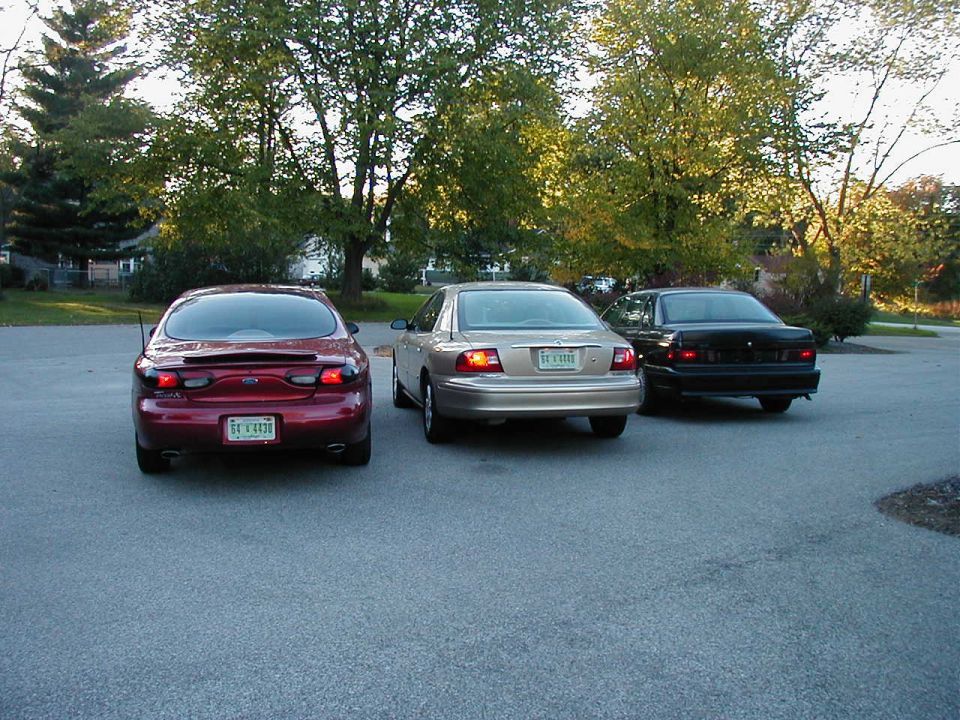 Red sedan, gold sedan, and black sedan parked in a lot. Red sedan has a license plate reading 'EE V 4438'