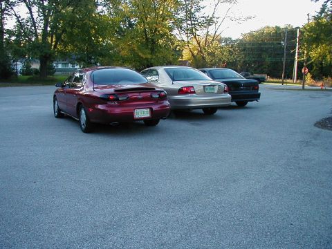 1990 Ford Taurus - Rear view of a red sedan parked in a lot with two other vehicles.