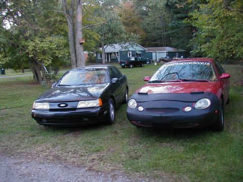 1990 Ford Taurus - Two Ford Taurus sedans are parked in a grassy yard with houses and trees in the background.