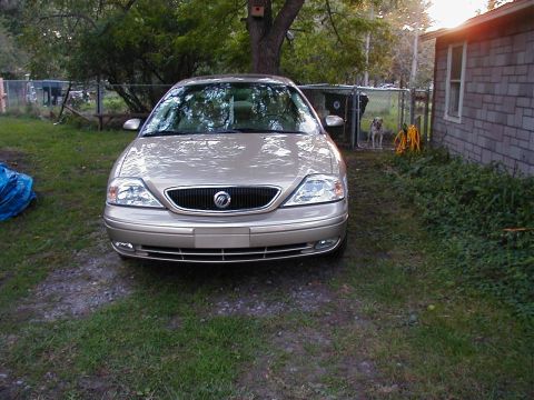 1990 Ford Taurus - A tan sedan is parked in a yard with a dog visible in a fenced area.