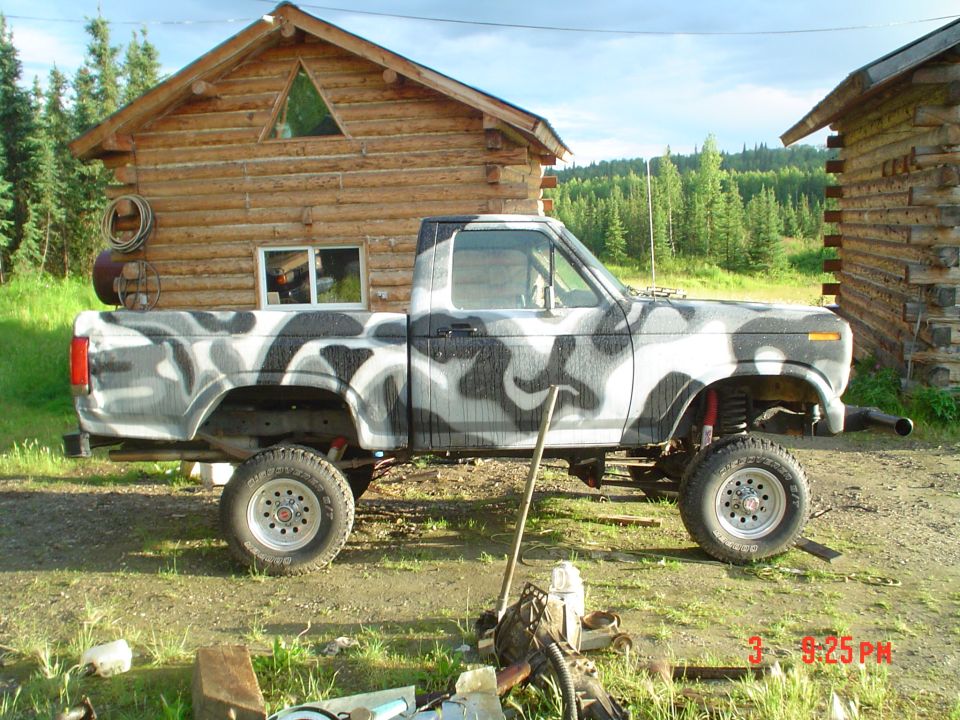 Pickup truck with camouflage paint job parked in front of a log cabin