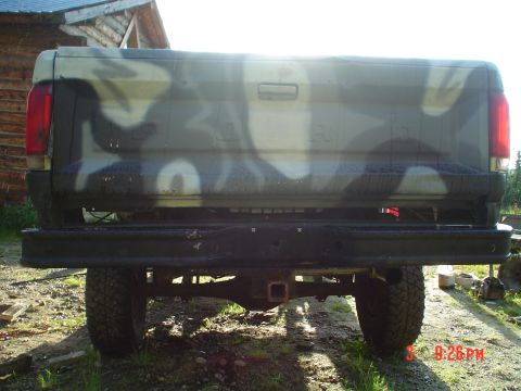 1986 Ford F-150 - Rear view of a camouflage-painted pickup truck, likely from the 1980s, a black bumper and tow hitch.