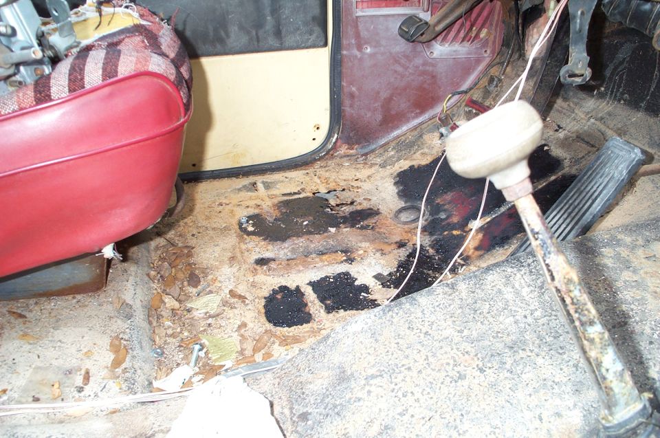 driver's side floorboard with rust and debris, red seat visible