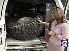 1993 Ford Bronco - Woman gestures towards a large off-road tire inside the cargo area of a van.