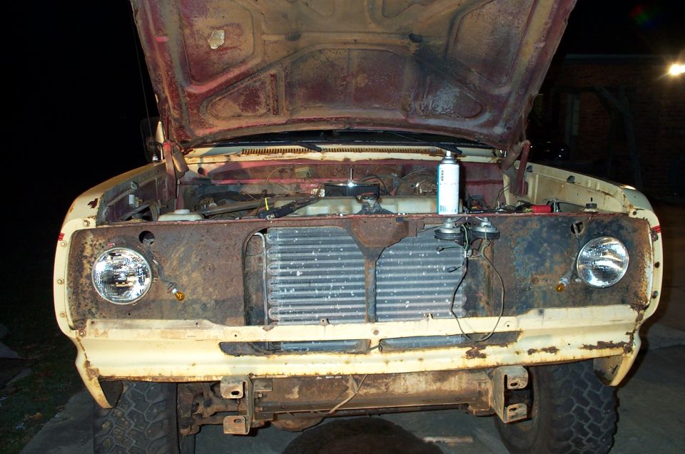 Rusty truck front end, hood open, showing engine bay and radiator. Cream and red paint