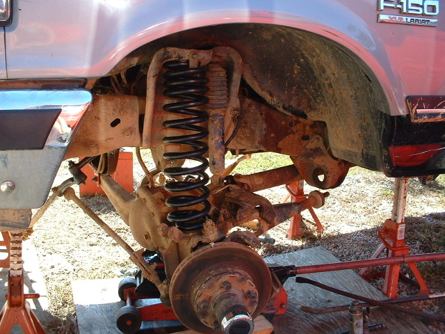 Front suspension of a 1987 Ford F-150 on jack stands, showing the coil spring, shock, and brake components
