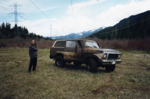 1979 Ford Bronco - A muddy 1979 Ford Bronco sits in a field, with power lines and mountains visible in the distance.