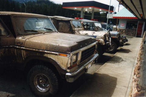 1979 Ford Bronco - Muddy off-road vehicles, including a 1979 Ford Bronco, are parked at a gas station after an outing.