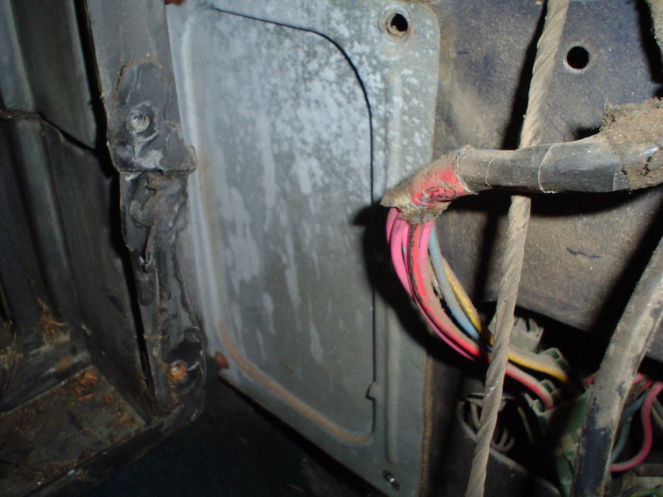 Close-up of a vehicle's interior wiring harness with red, pink, blue, and yellow wires connected to a metal panel