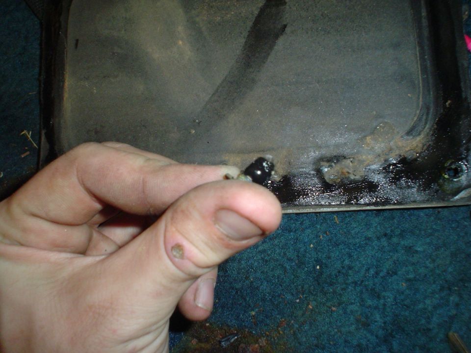 hand holding a black bolt near a metal surface with rust and grime