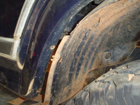 1984 Ford Bronco - Mud-caked wheel well of a blue vehicle, showing the tire and inner fender.