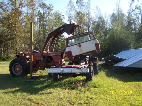 1976 Ford F-150 - A tractor is used to lift the cab off a truck chassis in a grassy yard.