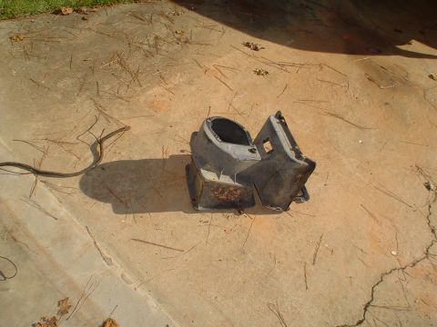 1984 Ford Bronco - A disassembled plastic component lies on a concrete surface, possibly removed from a vehicle for repair or replacement.