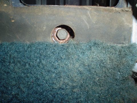 1984 Ford Bronco - A close-up view shows a rusty bolt securing the teal carpet in a vehicle's interior.