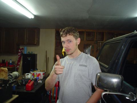 1984 Ford Bronco - A man points towards the camera in a garage setting, with a portion of a dark vehicle visible on the right.
