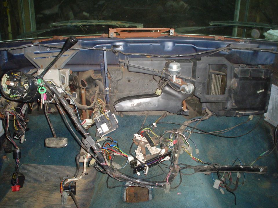 Vehicle interior dashboard with exposed wiring and components. Blue dashboard, teal carpet