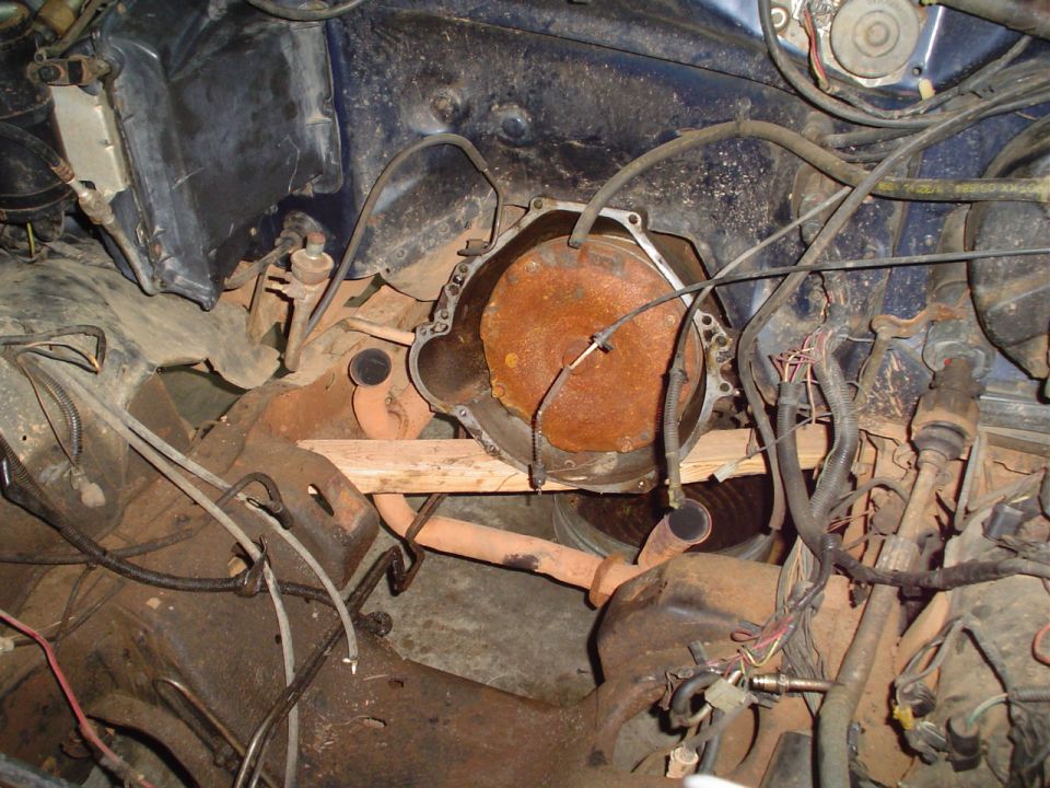 Engine bay showing transmission bell housing and rusty exhaust pipe