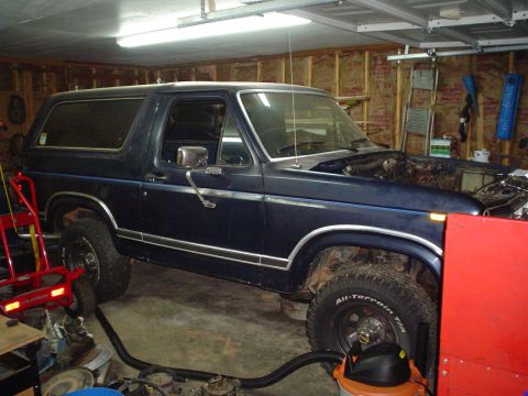 1984 Ford Bronco - Interior view of a dark blue Ford Bronco with the hood open, parked inside a garage.