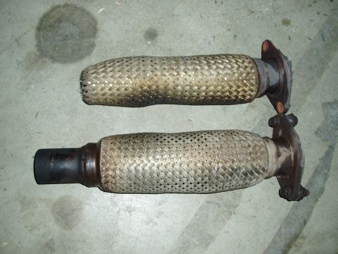 1993 Ford Taurus - Two exhaust flex pipes, one with a black end, lie on a concrete floor.