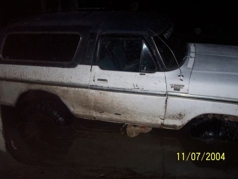 1979 Ford Bronco - A dirty white and black Ford Bronco is seen from the side, with its dark roof contrasting against the white body.