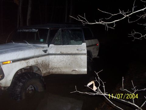 1979 Ford Bronco - A muddy 1979 Ford Bronco sits in the dark with its driver's door ajar.