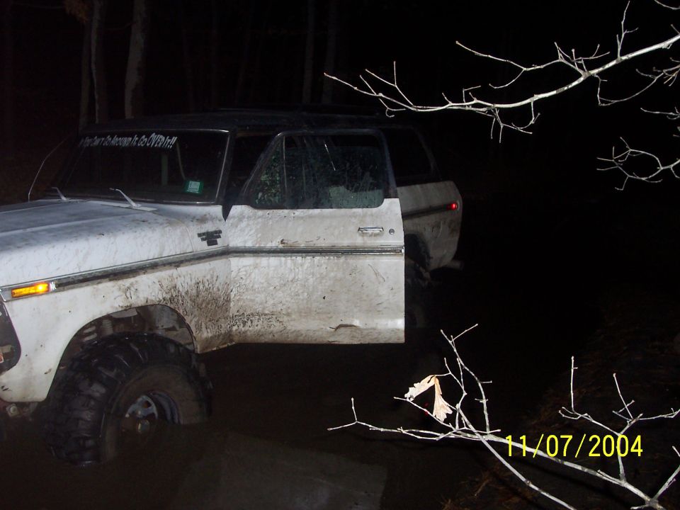 White 1979 Ford Bronco with open door, covered in mud