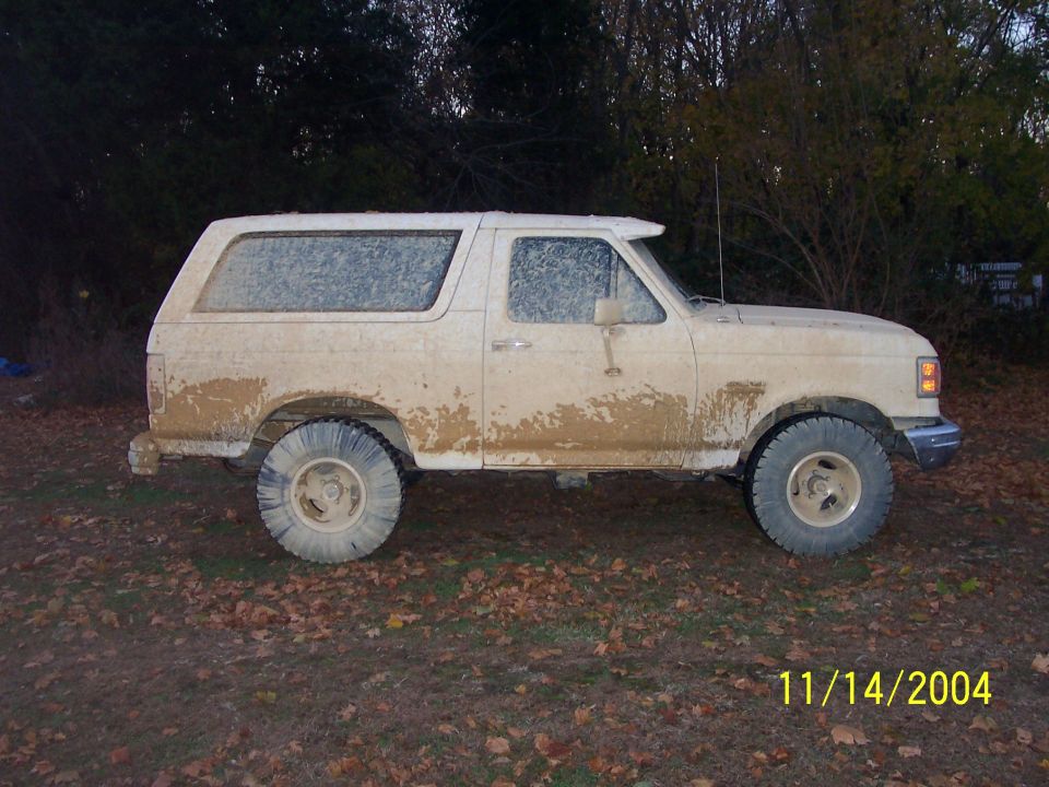 White SUV covered in mud, side view. Appears to be a 1980s Ford Bronco