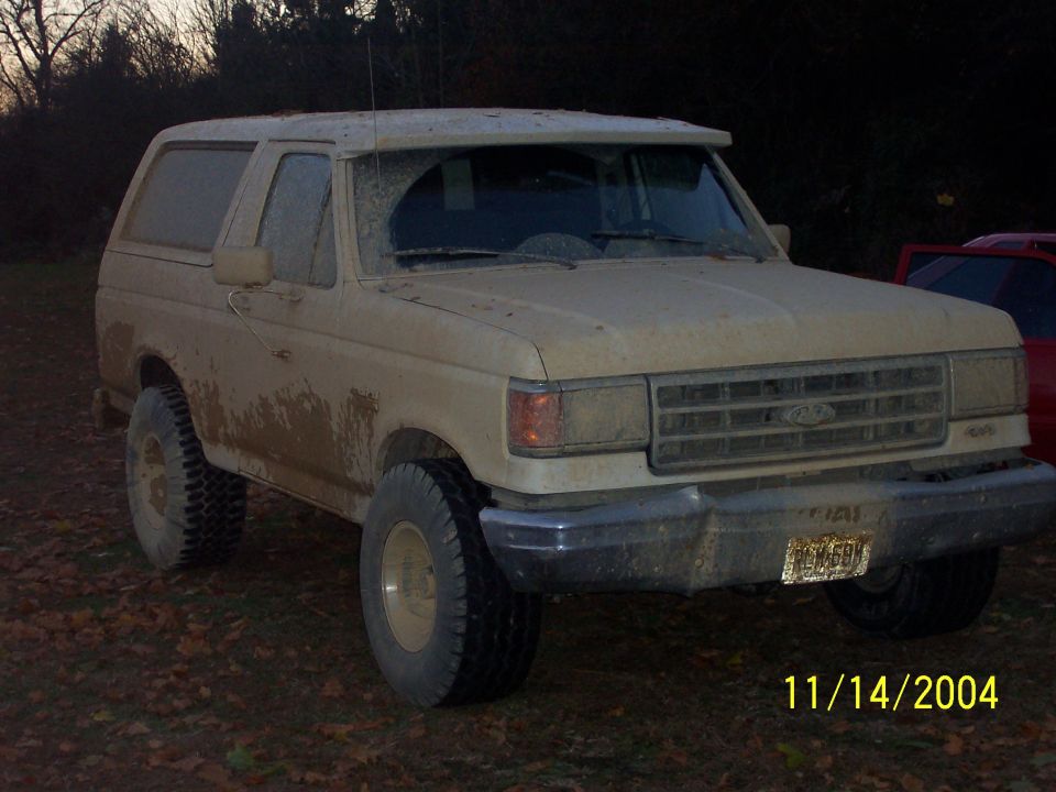 Tan Ford Bronco, 1987 model year, covered in mud, 3q front view