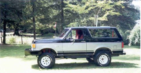 1989 Ford Bronco - A two-tone black-over-silver full-size Ford Bronco SUV shown in side profile, lifted on white steel wheels with BFGoodrich All-Terrain tire…