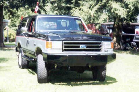1989 Ford Bronco - This two-tone Ford Bronco is parked on a grassy lawn with trees in the background.