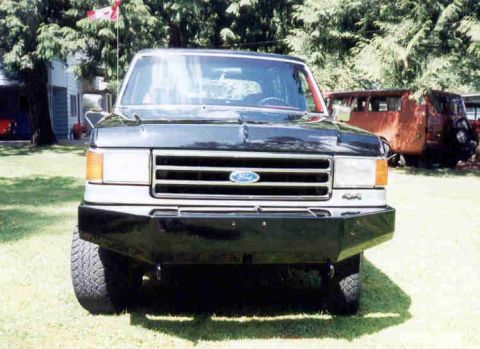 1989 Ford Bronco - Front view of a two-tone black-over-silver Ford SUV parked on grass, showing the chrome grille with blue Ford oval, dual round headlights,…