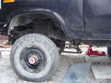 1986 Ford F-150 - Close-up view of the front driver side suspension and wheel of a truck, showing modifications.