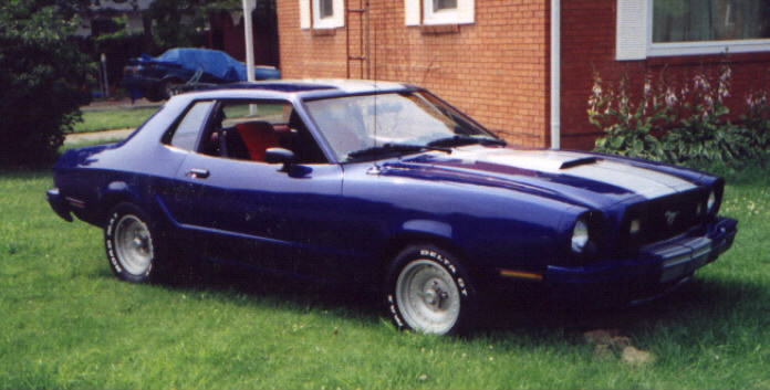 Blue 1977 Ford Mustang II coupe with silver racing stripes parked on grass