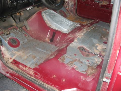 1991 Ford Bronco - The interior floor of a vehicle shows significant rust and exposed metal, with pedals visible in the driver's area.