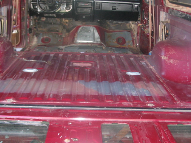 Interior of a red vehicle with seats and carpet removed, showing the floor and dashboard