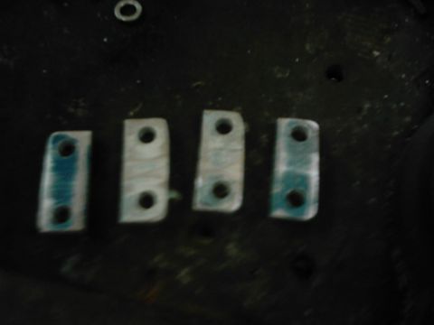 1978 Ford Bronco - Four metal brackets with two holes each are laid out on a dark surface.