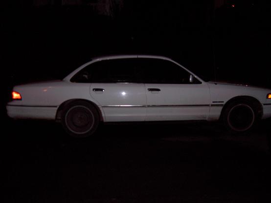 White full-size four-door sedan photographed in profile at night with headlight on