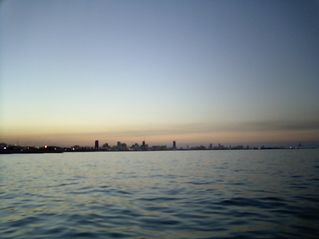 City skyline visible across water at dusk with a faint Supermotors logo in the lower right corner