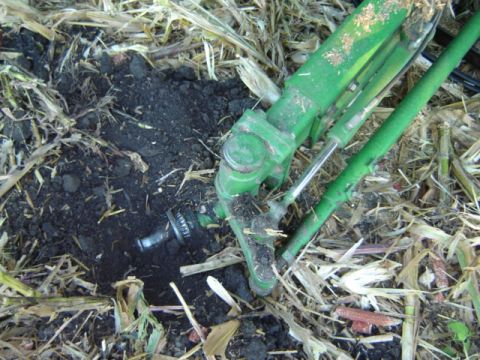 1992 Ford Bronco - Tractor hydraulic part buried in the dirt with crop residue around it.