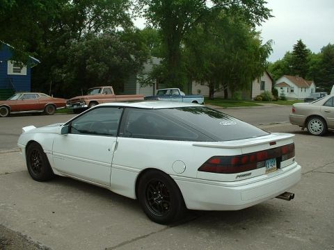 1992 Ford Probe - A white 1992 Ford Probe is parked on a residential street with other vehicles and houses visible.