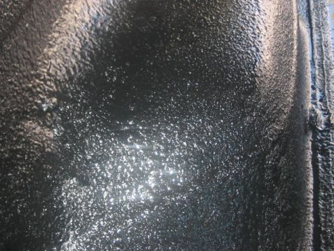 1991 Ford Bronco - The textured black undercoating on a vehicle's undercarriage shows some reflective moisture.