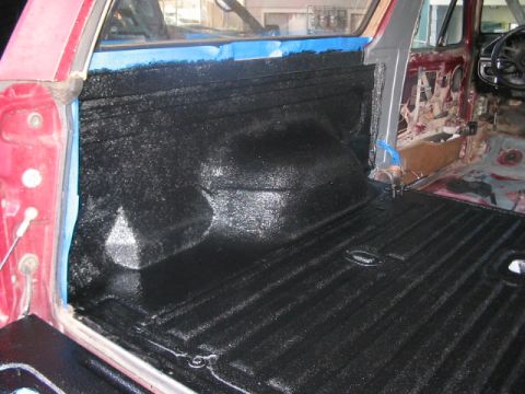 1991 Ford Bronco - The interior of a red vehicle is being treated with black spray-on bed liner, with blue tape applied to the door frame.