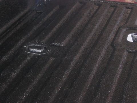 1991 Ford Bronco - Close-up of a black truck bed liner showing its textured surface and a metal tie-down anchor point.