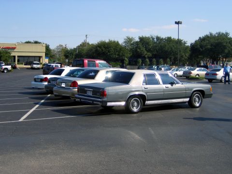 2000 Ford Crown Victoria - Several cars are parked in a lot on a sunny day, with a gray Ford Crown Victoria in the foreground.