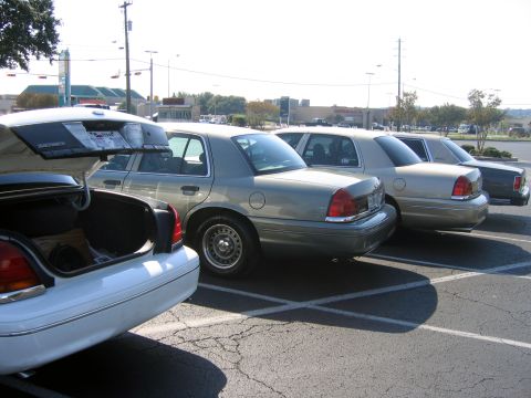 2000 Ford Crown Victoria - Several Ford Crown Victorias are parked in a lot, with one in the foreground showing its open trunk.