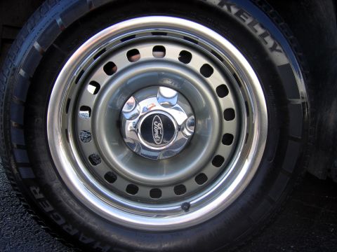 2000 Ford Crown Victoria - Close-up of a green-painted steel wheel with a polished outer lip, slotted vent holes and a chrome five-lug Ford center cap. It is mounted…