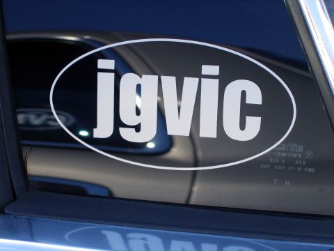 2000 Ford Crown Victoria - Close-up of a white oval euro-style decal reading "jgvic" applied to the tinted rear side window of a dark blue car. The Carlite tempered-g…